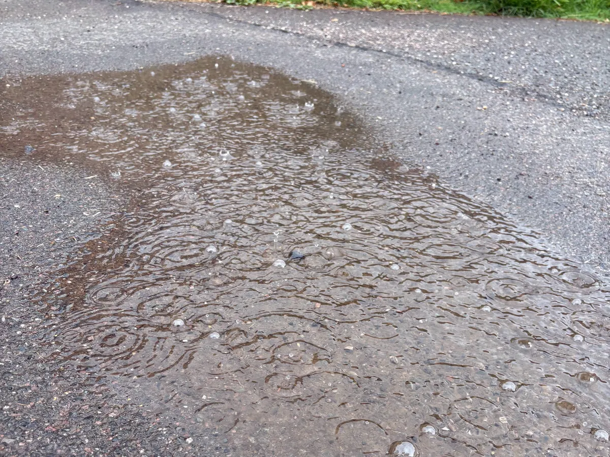 Close-up of wet path with raindrops falling into puddle, creating ripples and splashes
