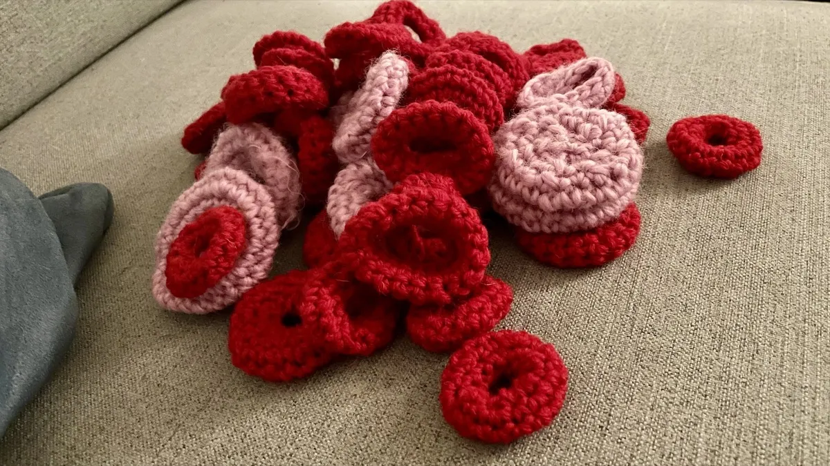 A pile of crocheted cat bagel toys in red and pink on a greige fabric couch.