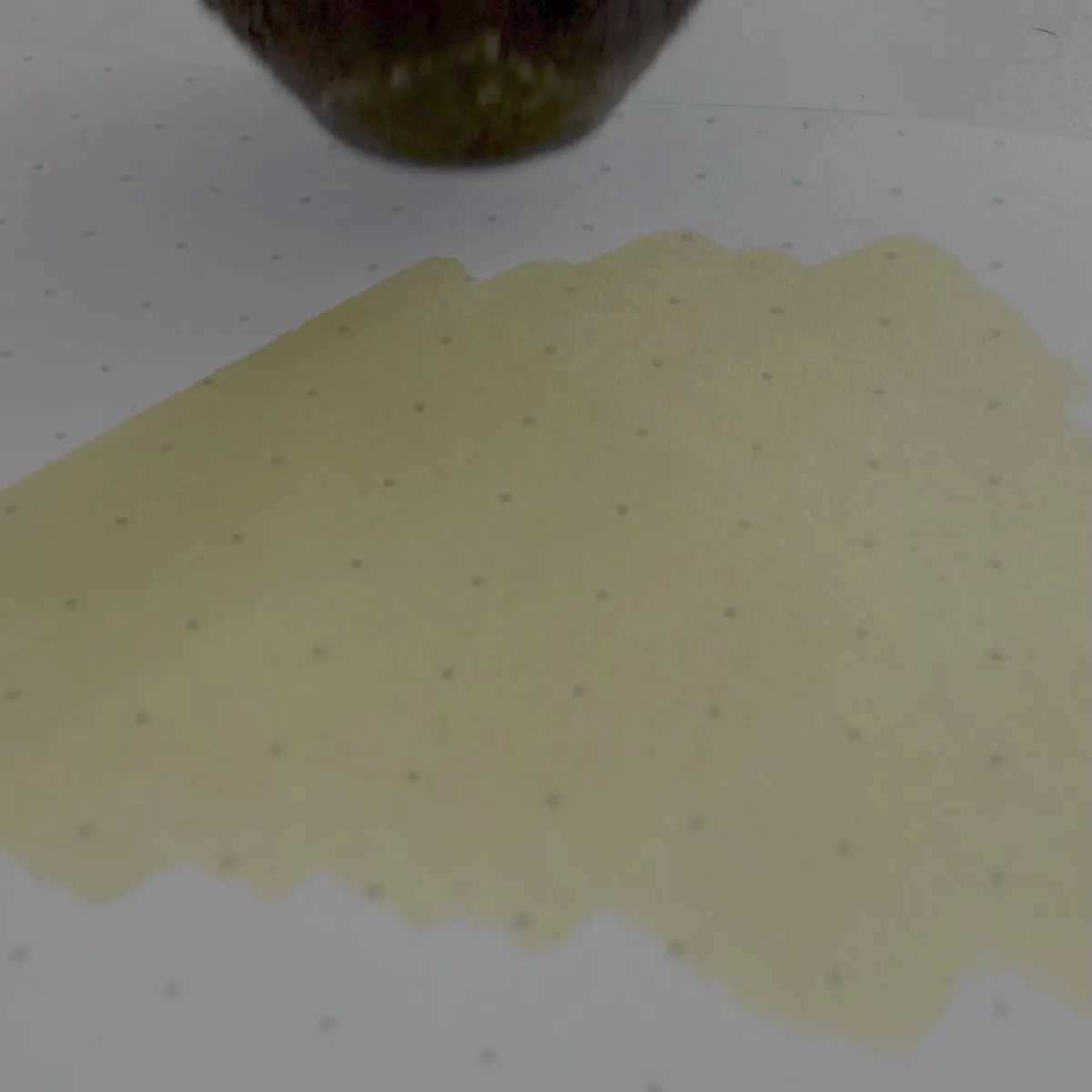 A swatch of yellow ink on dotted Rhodia paper. At the top of the image, part of a dark-brown, almost black, cat chin is just visible, suggesting cat help.