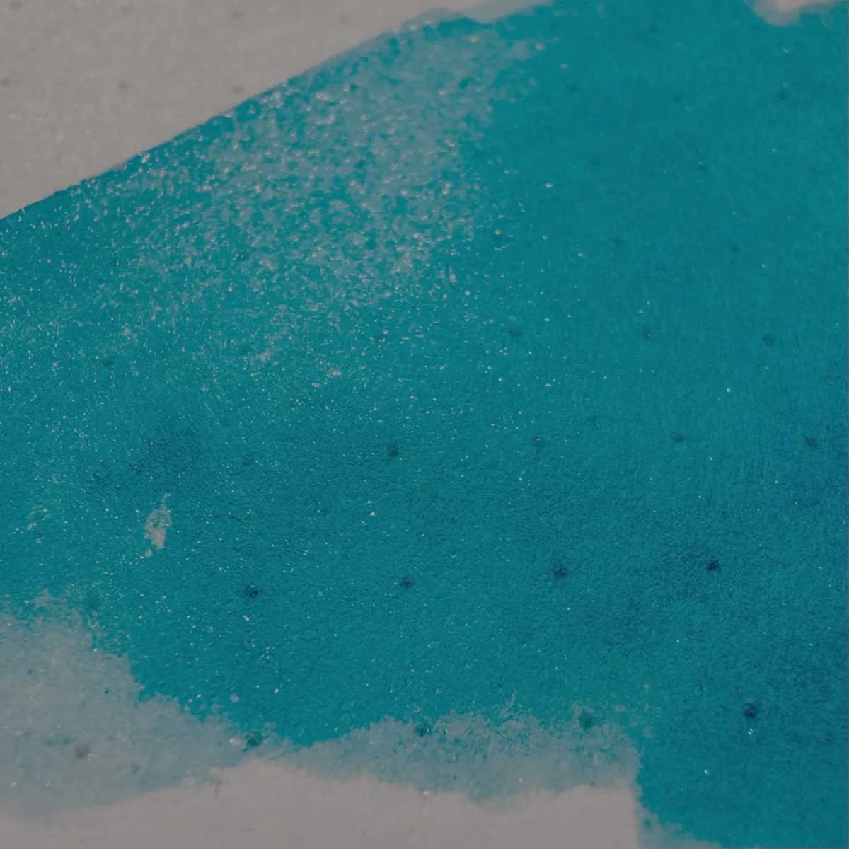 A close-up of a bright turquoise blue ink swatch on white, dotted Rhodia paper. The colour varies in intensity, with some lighter and darker areas, and some silvery-blue shimmer visible.