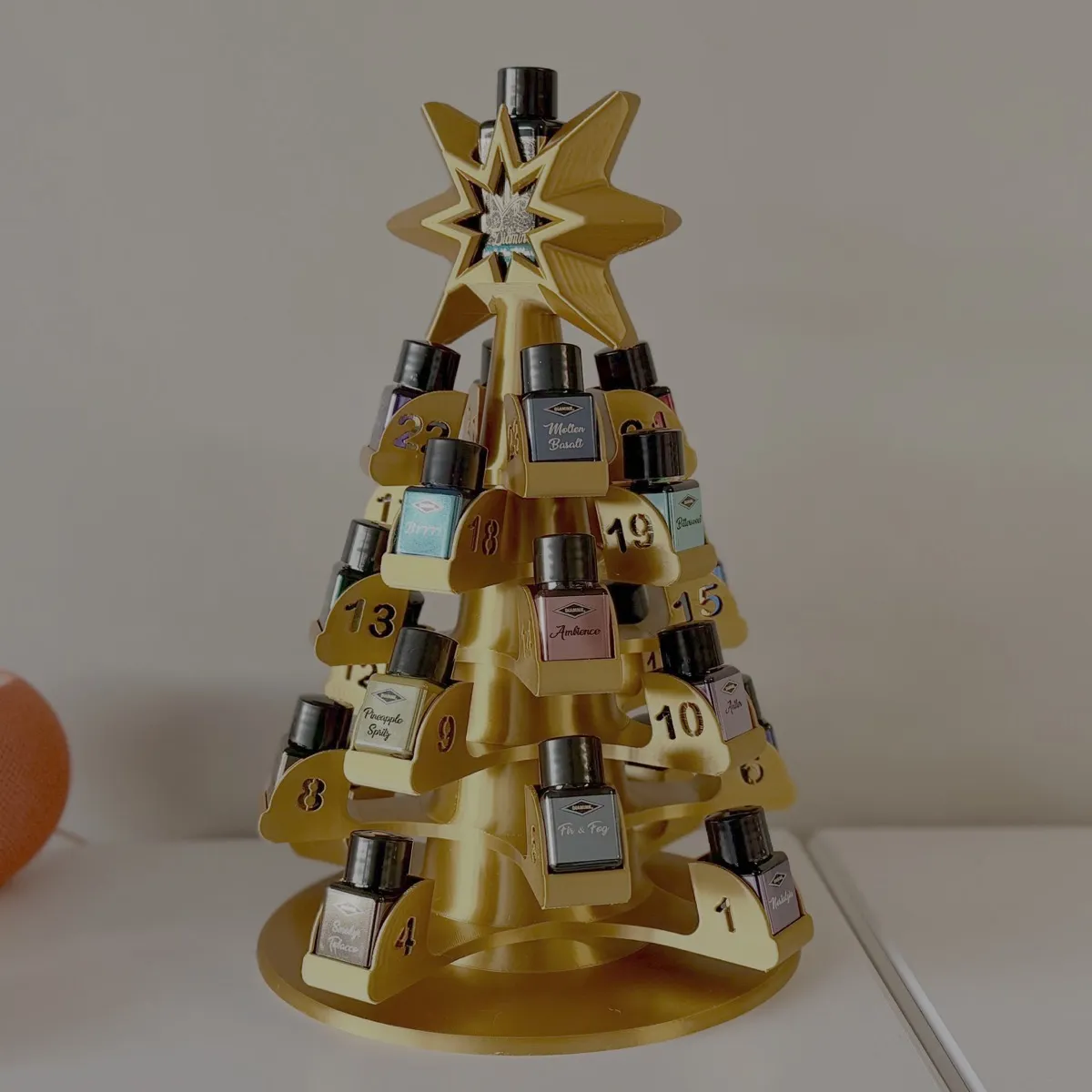Golden 3D-printed tree-shaped advent calendar holder for the Diamine Inkvent bottles. The tree has numbered shelves from 1 to 24, each containing a small bottle of ink. The tree is topped with a star decoration, which also holds the large bottle revealed on the 25th.