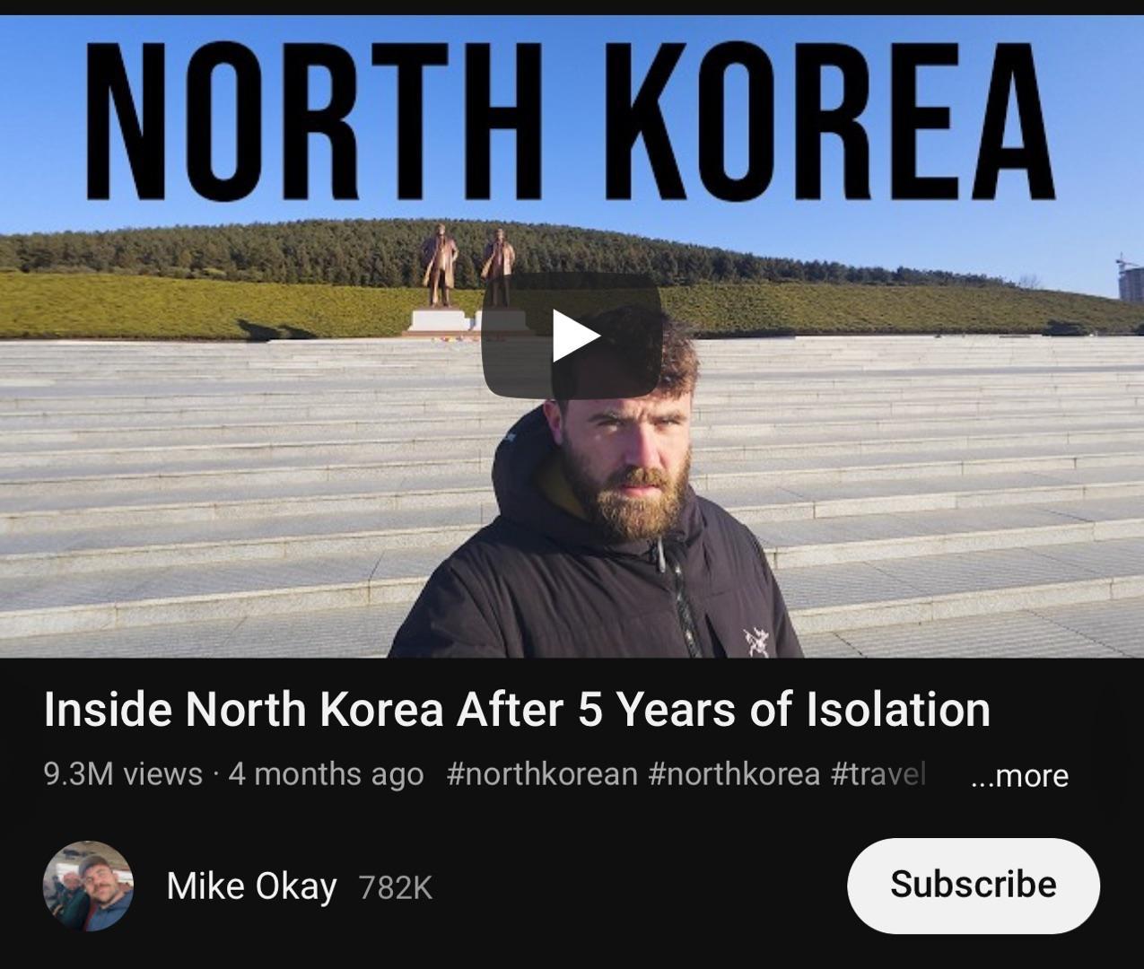 A video thumbnail displays a man standing on a set of wide, stone steps, under a large blue banner reading "North Korea". The man is looking directly at the camera, wearing a dark, hooded jacket, and has a full beard. In the background, two statues are visible atop a green hill, with a clear blue sky above. The video's title, "Inside North Korea After 5 Years of Isolation", suggests a look into the country's state following a period of isolation. The thumbnail also includes a play button icon and a view count of 9.3 million, indicating the video's popularity. _ Description generated by piccybot.com 🤖