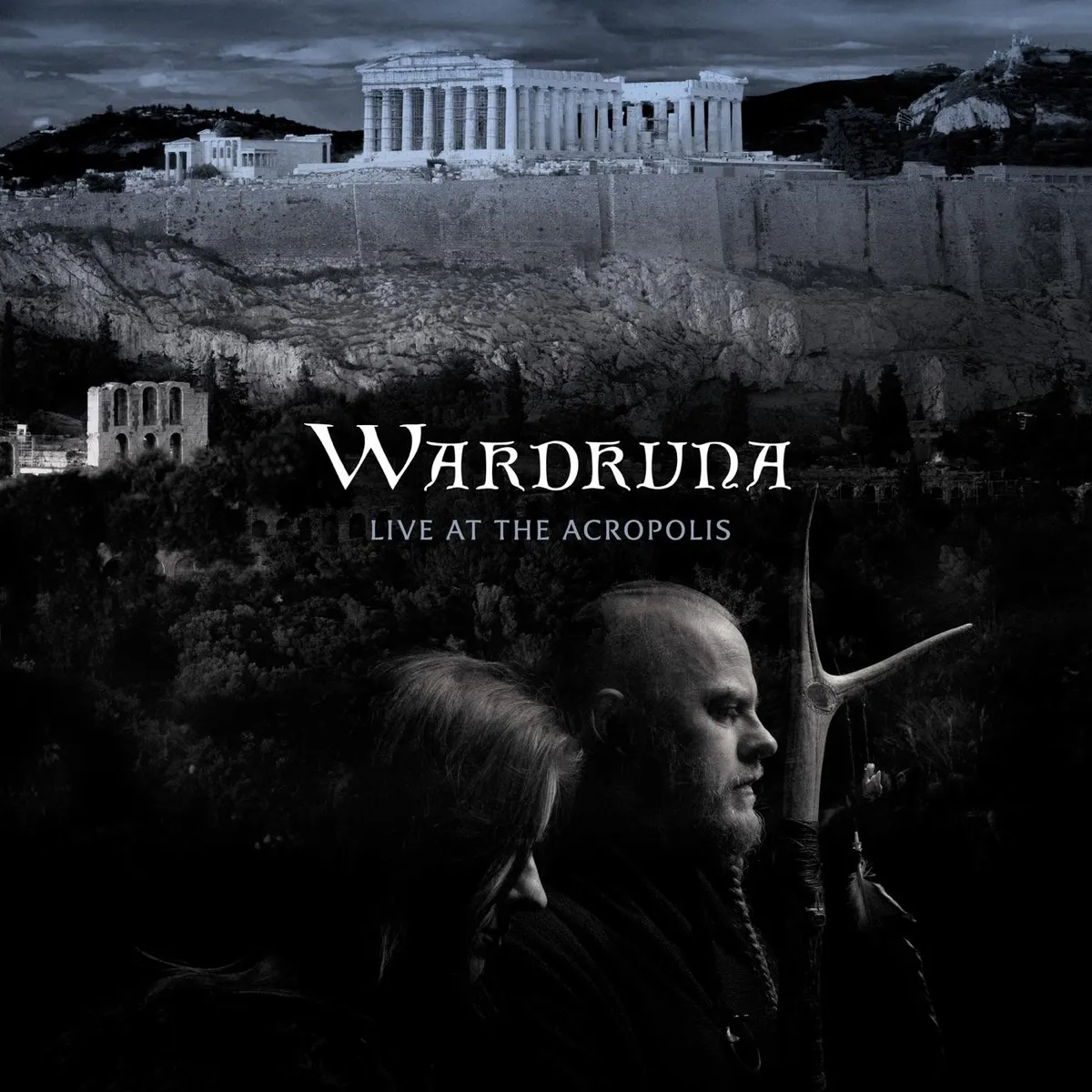 A black and white album cover featuring two figures in profile against a dramatic backdrop of the Parthenon atop the Acropolis in Athens. Set against stormy skies and ancient Greek architecture. Text reads Wardruna Live At The Acropolis