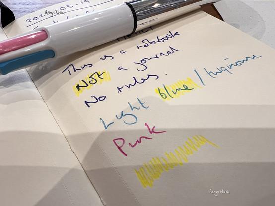 A close-up photo of some handwritten text in various colours in a notebook with a pen sitting on top.