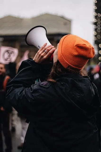 A person in an orange hat shouts through a megaphone