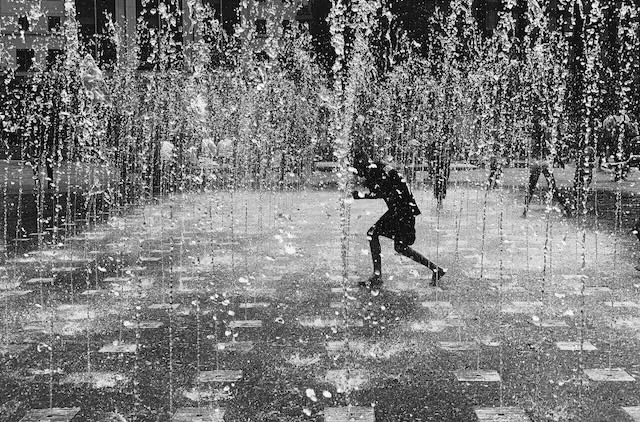 A boy runs through fountains in black and white