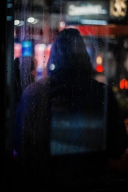 A hodded figure is pictured through the rainy window of a bus stop