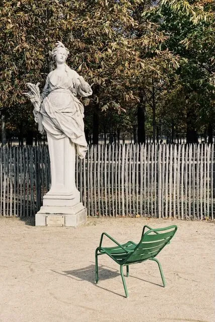 A parisian statue regards a lone green chair