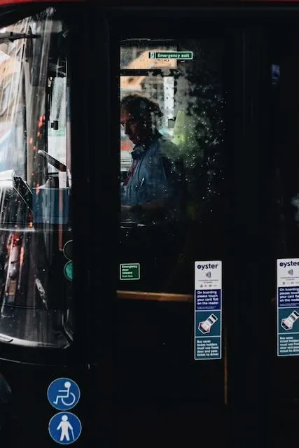 A busdriver is seen through a window smattered with rain