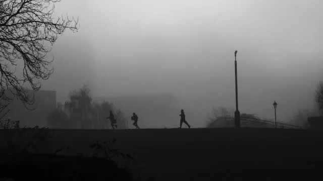 Three children run through thick fog in a park