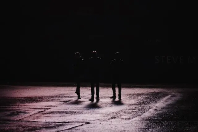 a trio of people walk through a pool of light at night