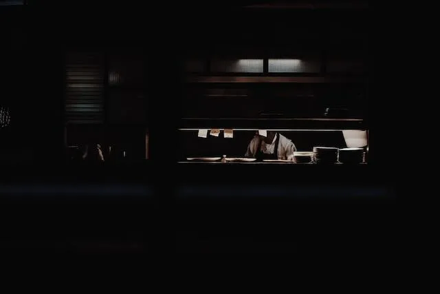 A cook can be seen through the thin frame of a gantry in a dark restaurant
