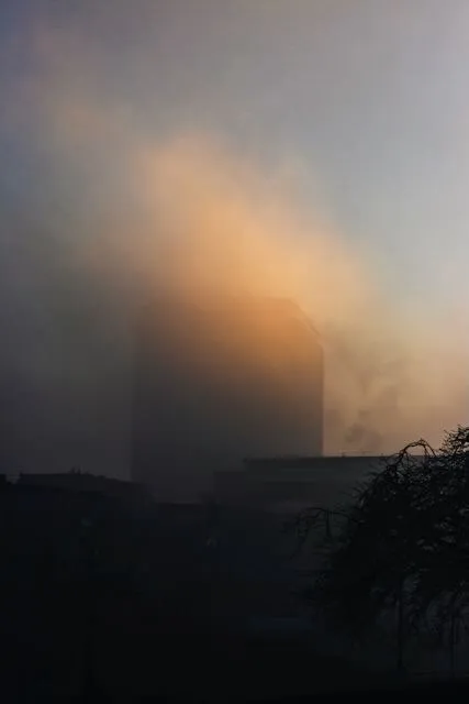 a building partly obscured by a strange swipe of fog glowing orange from the evening light