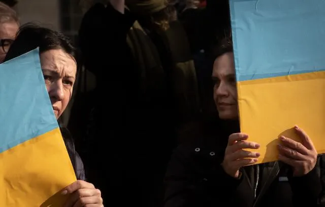 Two women hiding behind Ukrainian flags