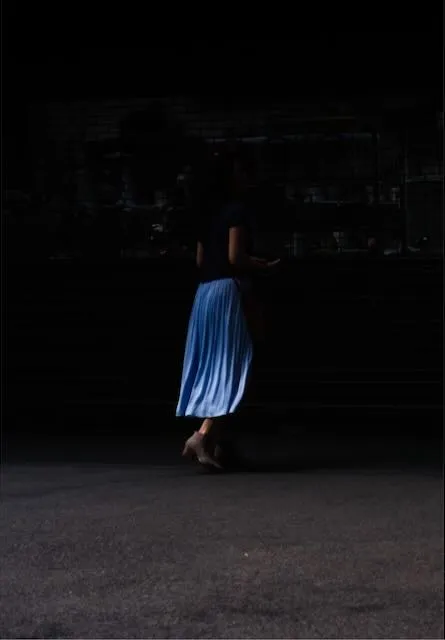 A woman emerging from the darkness in a blue skirt