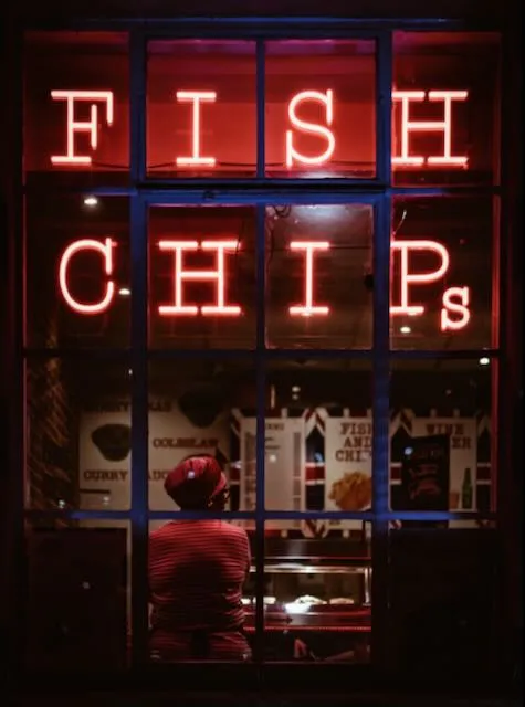 A neon fish and chips sign at night