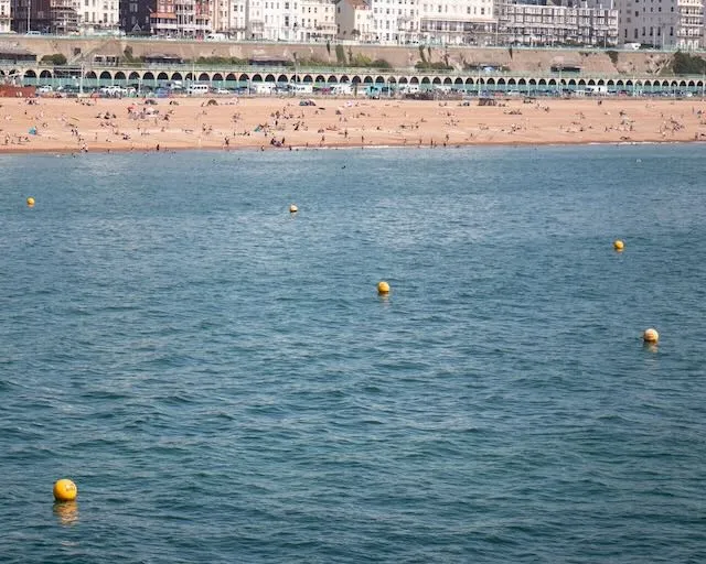 Yellow buoys float in a blue sea, a beach covered in tourists can be seen in the distance