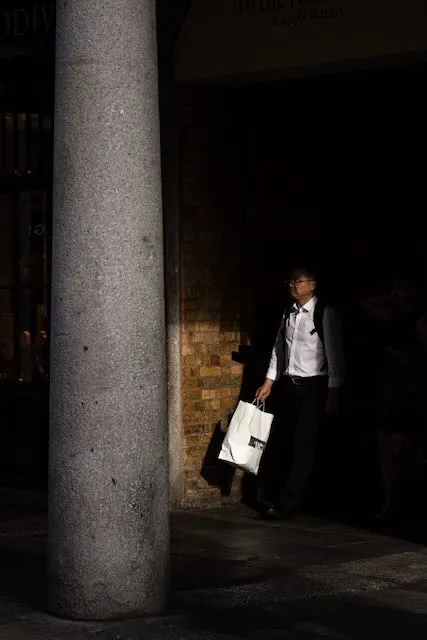 A man walks out of the darkness holding a paper bag