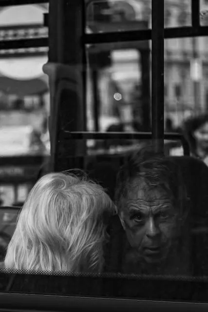 A man peers through a bus window directly into the camera