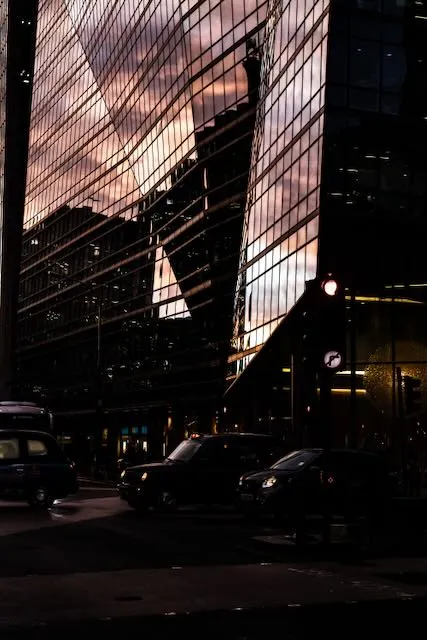 A building reflects the sunset as black cabs pass below