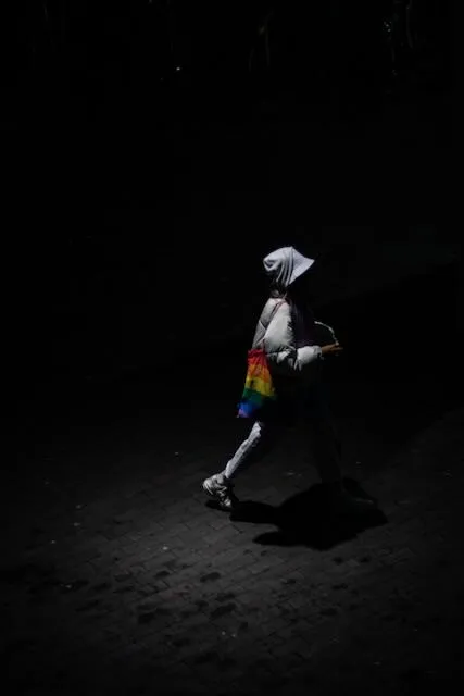 a woman passes through a patch of light carrying a rainbow tote bag