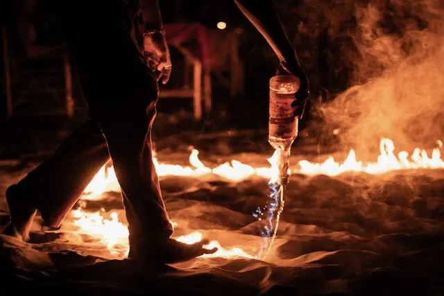 A man pours fire from a bottle onto the sand