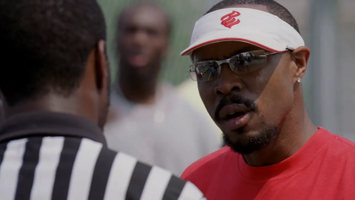 Avon yelling at the ref in the projects basketball game, who is reflected in his sports glasses, alongside the rival coach.
