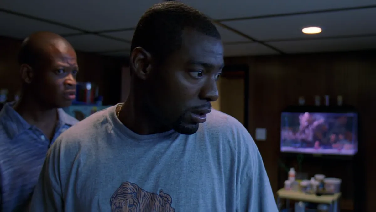 Wee Bey looking at his fish tanks while D looks at him skeptically in the background.