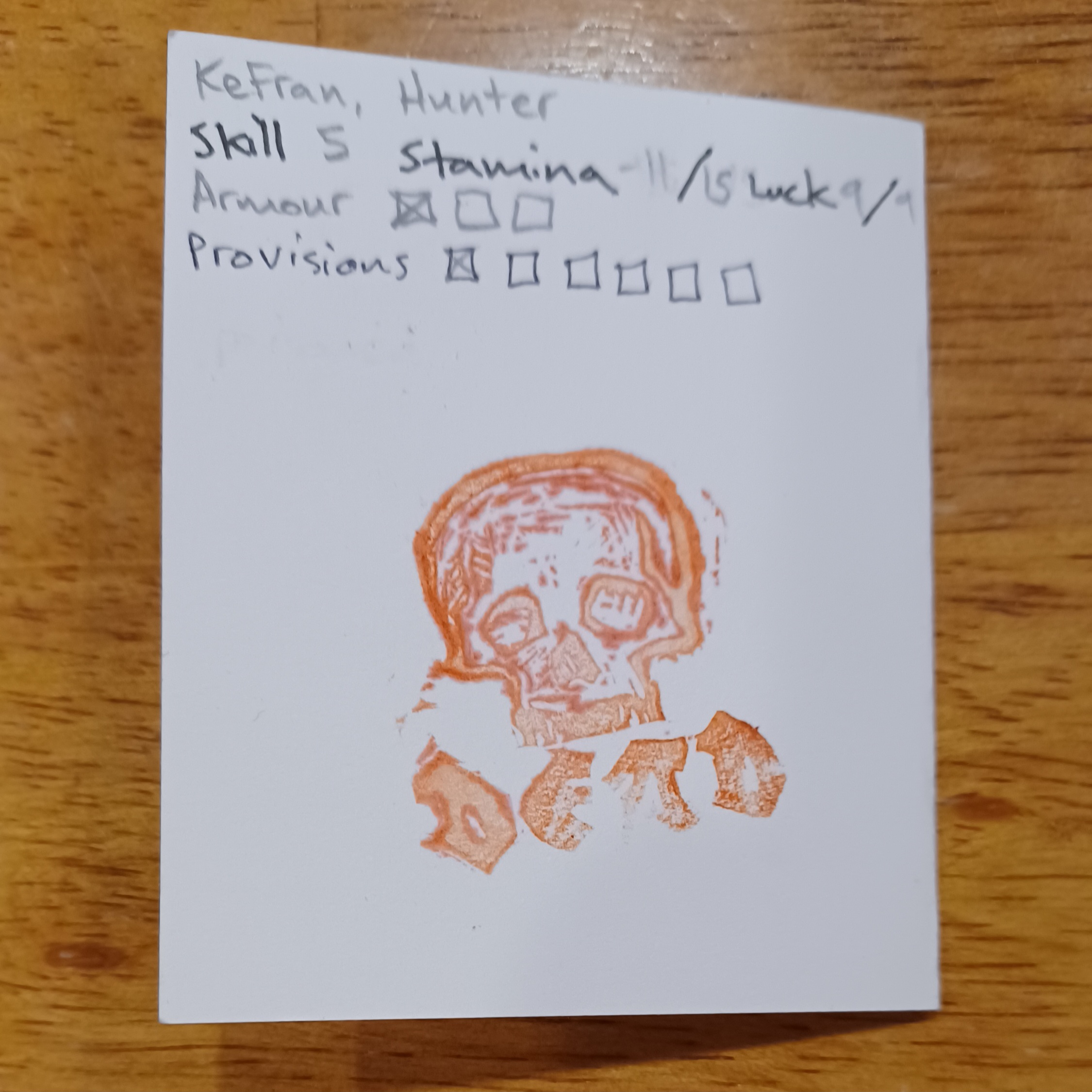 A photo of a folded index card that served as a Troika! character sheet. There is a red stamp mark on the sheet: a skull and the word DEAD.