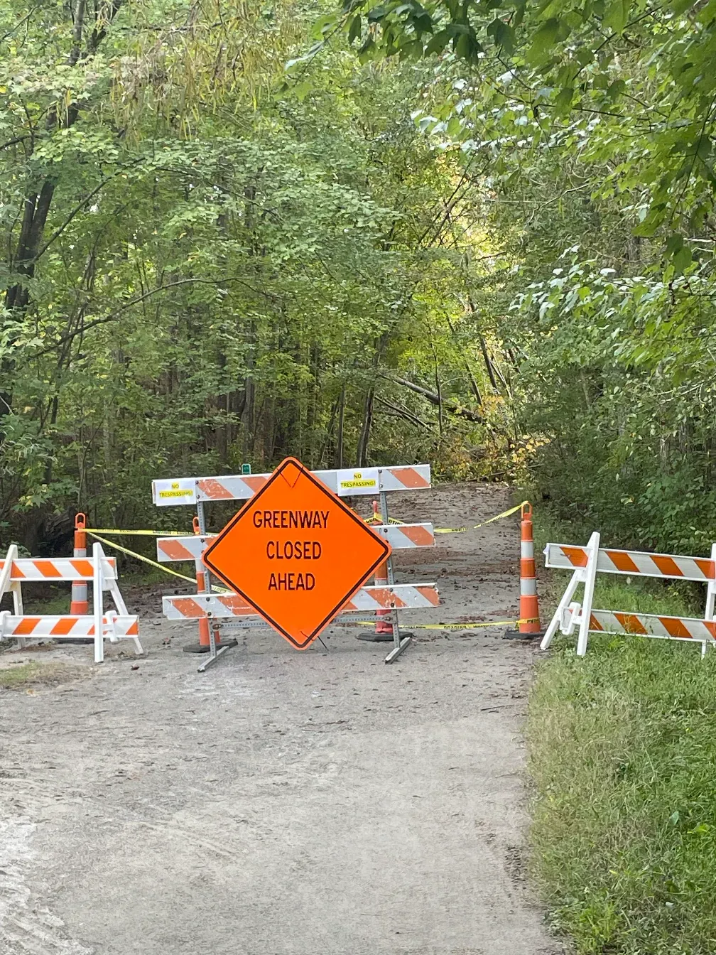 A "greenway closed ahead" sign in front of fallen branches.