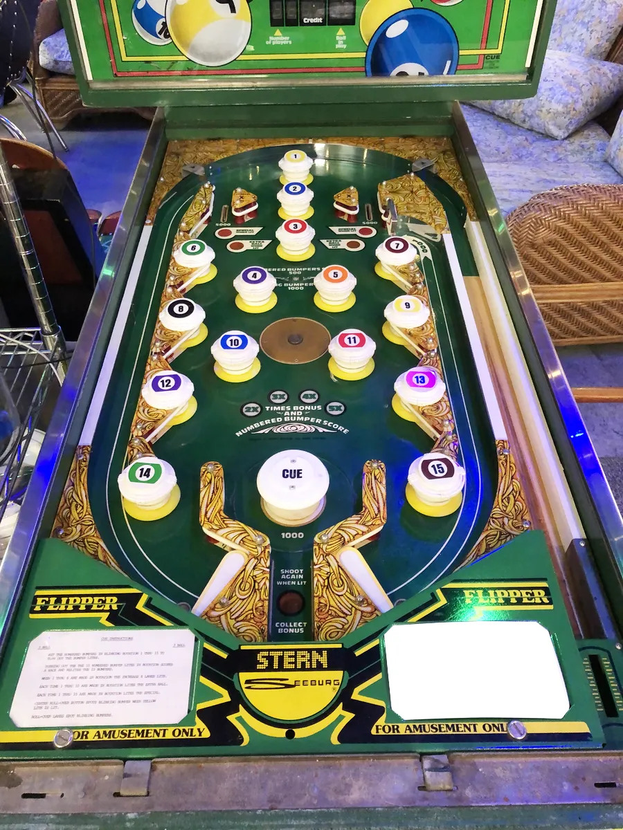 The playfield of Cue, mostly numbered pop bumpers. The only flippers point backwards where you'd expect outlanes to be.