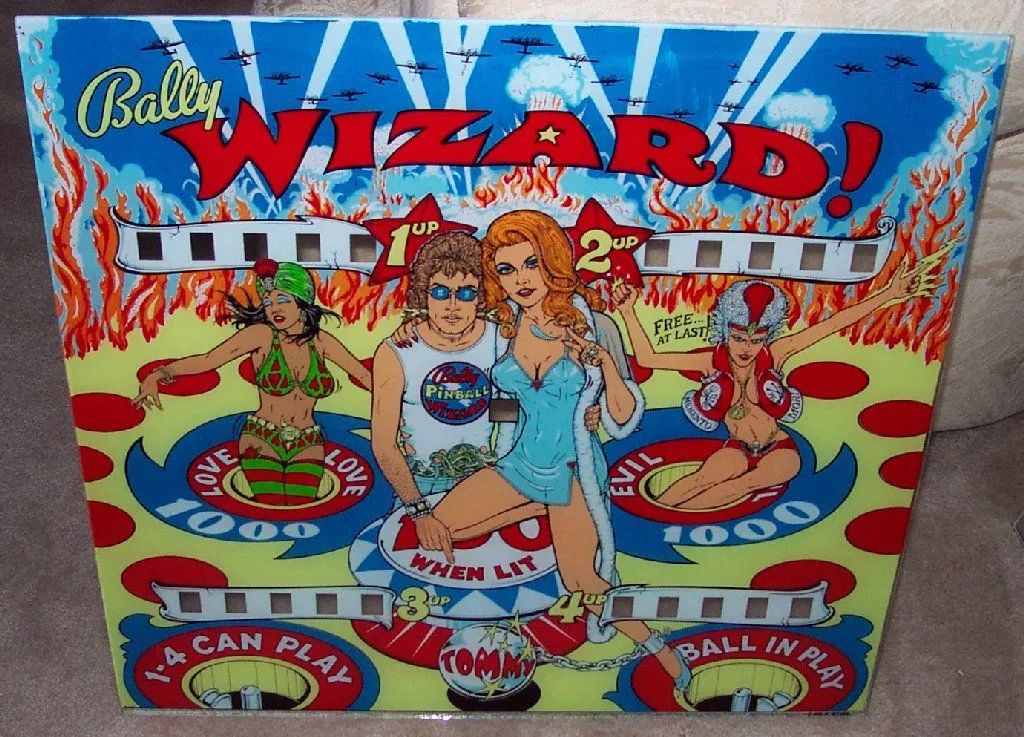 The backglass of Bally's "Tommy". Bomber planes fly above a fiery, hellish scene where Roger Daltrey embraces Ann-Margret. Two other sexy women emerge from pinball saucers, one of them saying "FREE AT LAST".