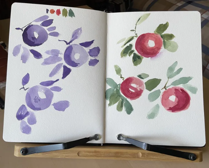 A sketchbook spread of apples painted in dioxazine purple on the left and a mix of reds and greens on the right.