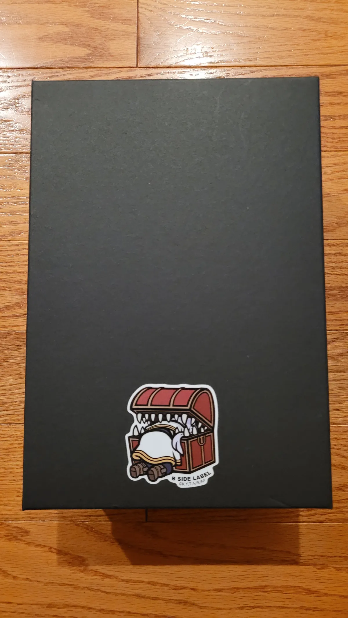 A shoebox with a sticker of Frieren stuck in a treasure chest with teeth.