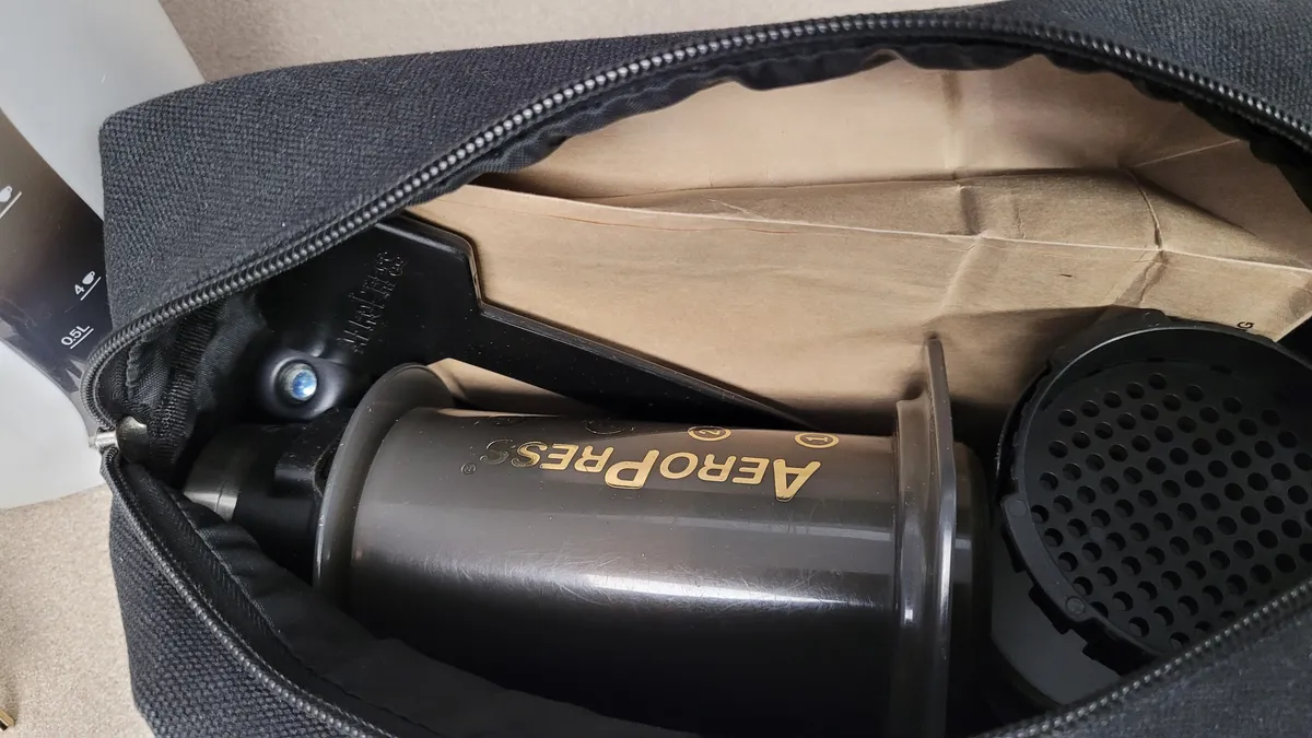 a canvas bag containing an AeroPress, Porlex mini, and bag of coffee beans