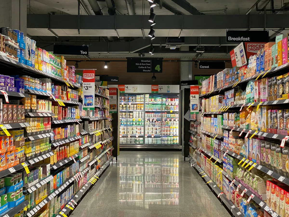 The Option Bomb A wide-angle view down a brightly lit grocery store aisle, with shelves stacked high on both sides with hundreds of different colorful boxes, representing the overwhelming number of choices that can lead to decision fatigue.