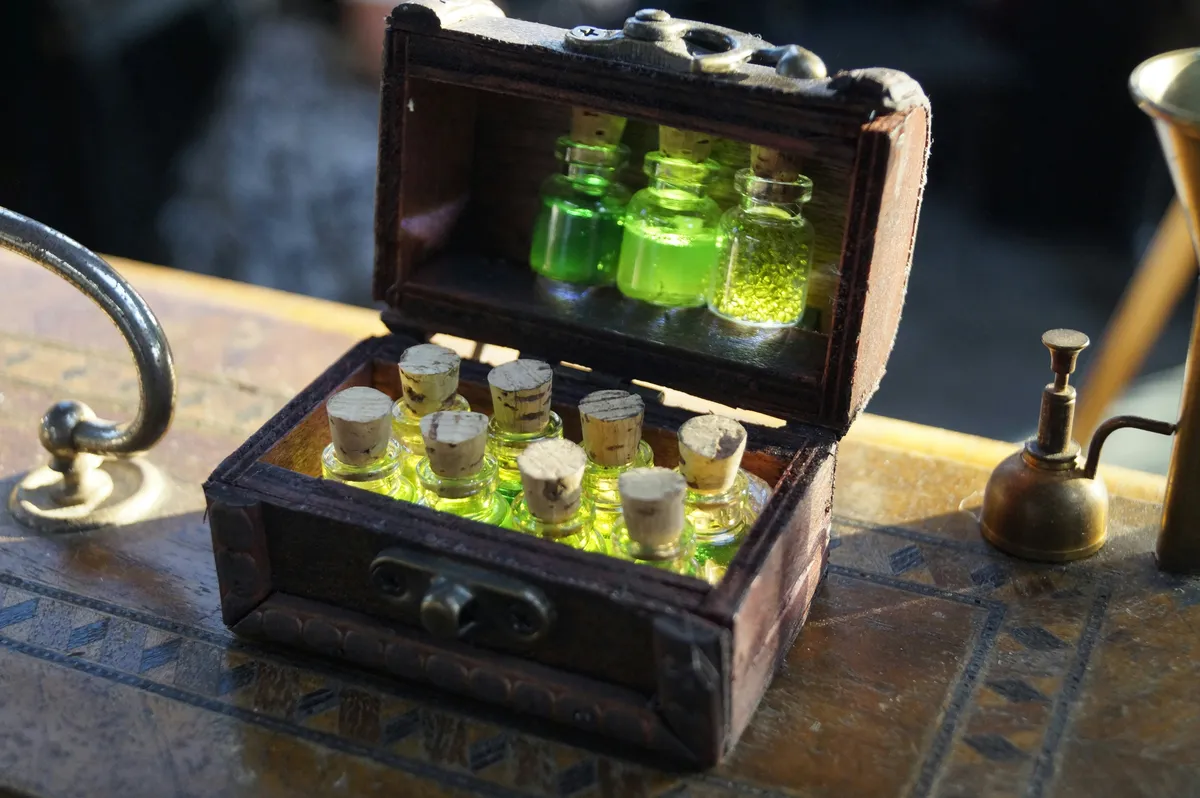 An Alchemist's Toolkit A small, open wooden chest on an ornate table, filled with rows of tiny glass bottles containing a glowing yellow-green liquid and sealed with corks.