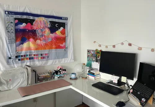 desk in L shape with laptop, external screen, crafting supplies, and a huge tapestry that shows a Paint95 interface with a big space jellyfish surrounded by clouds