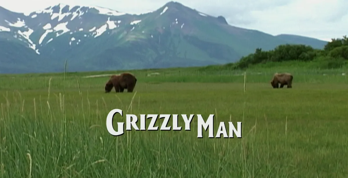 Title screen for Grizzly Man. The text is set against a green pasture with two bears grazing on the field.
