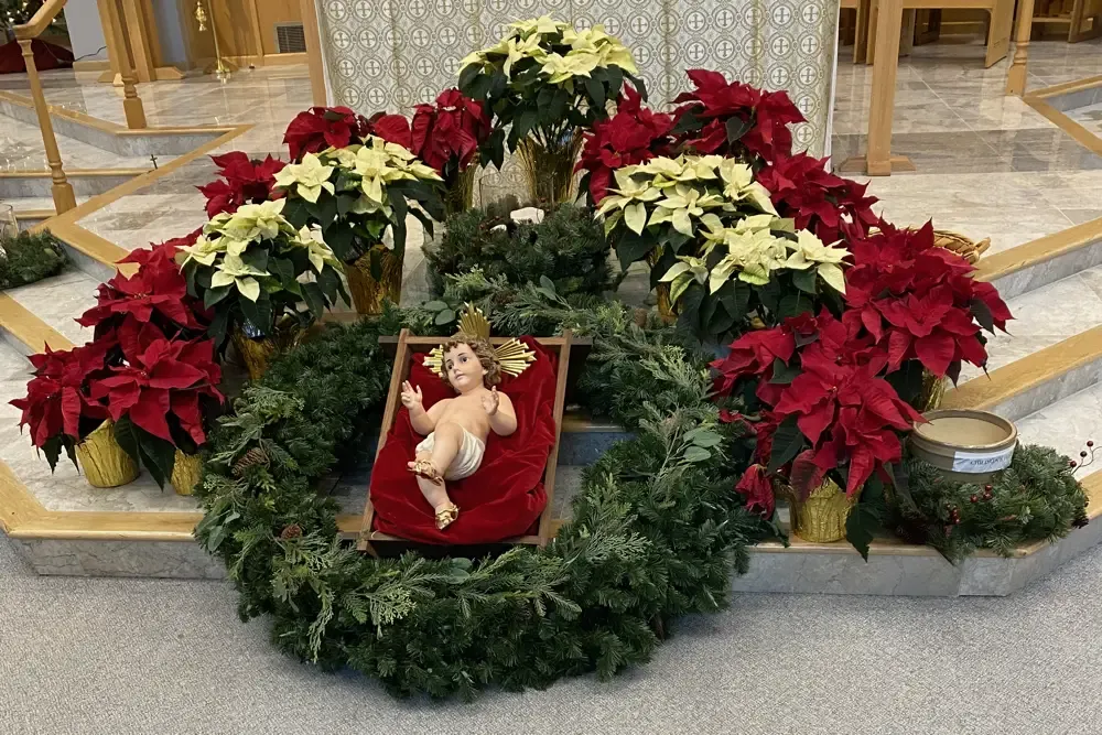 Baby Jesus altar display surround by a wreath and flanked by a mix of red and white poinsettias.