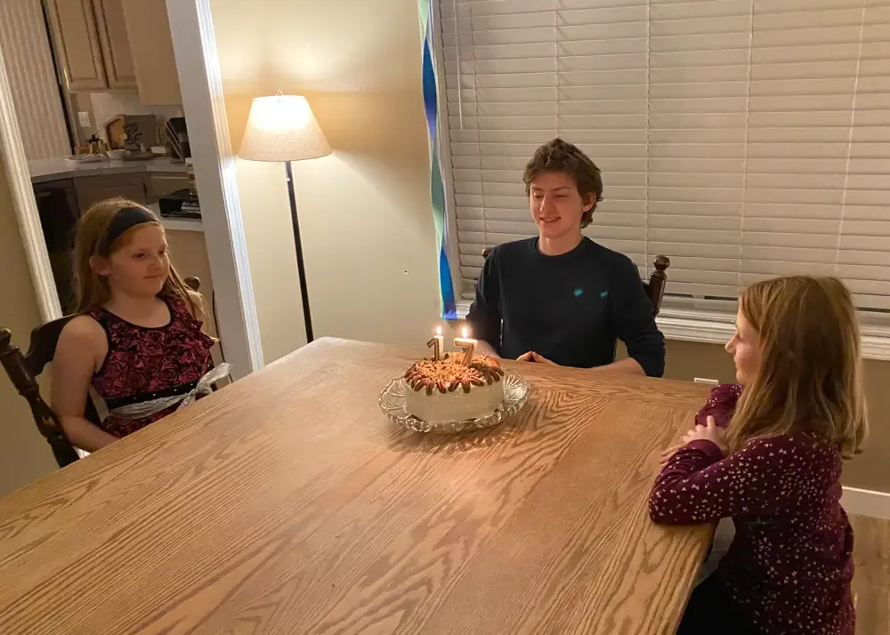 Nathan gazes at the birthday carrot cake he baked for himself as L and J look on.