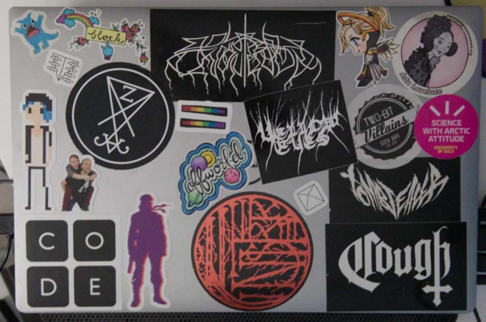 A laptop covered in stickers, mostly of black metal bands