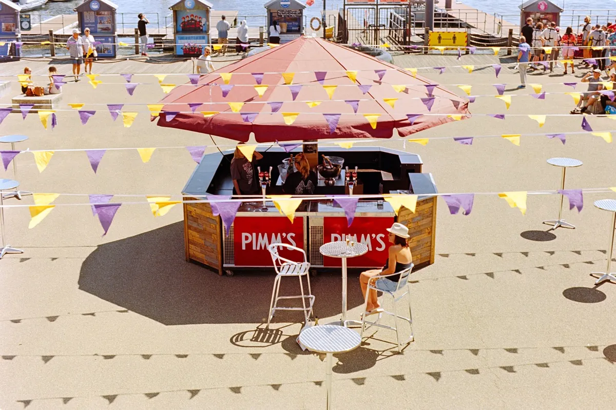 A woman sat in the sun beside a Pimms stand