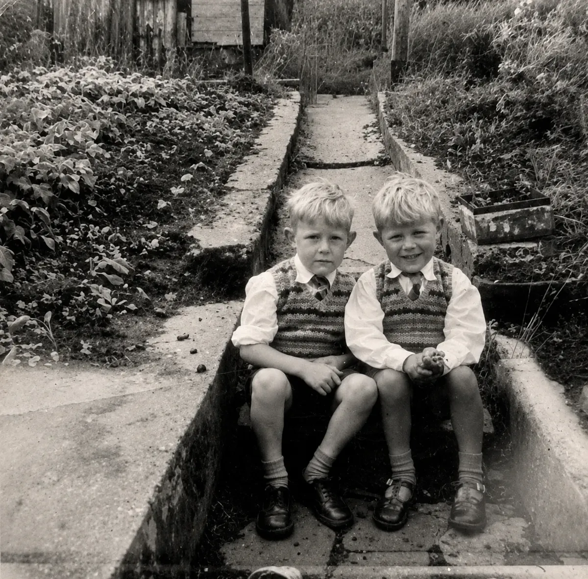 Two 5 and 6 year old brothers sitting on the back step dressed in their Sunday best in the late 1950s.