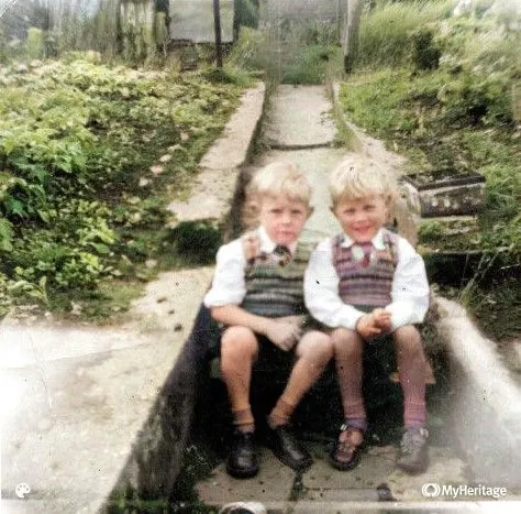 A colourised version of two brothers sitting on back garden steps. The photo was taken around 1960