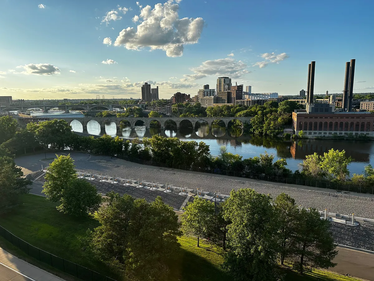 A photo of Minneapolis showing the Stone Arch Bridge on a sunny summer day with a few clouds