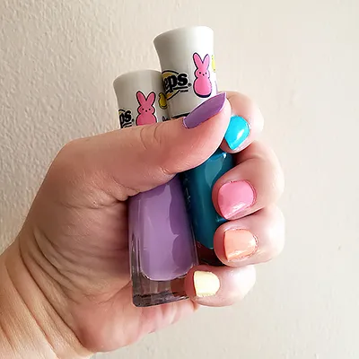 two bottles of 'Peeps' nail polish held in one hand; each fingernail is painted a different pastel shade
