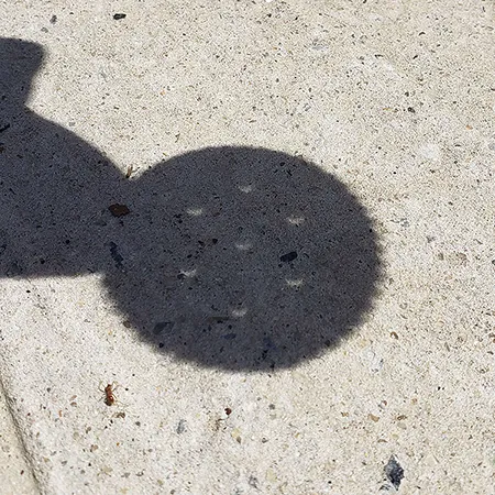 a shadow showing a person (me) holding out a Ritz cracker; each of the five holes in the Ritz cracker display a crescent shape instead of a circle, showing the ongoing eclipse.