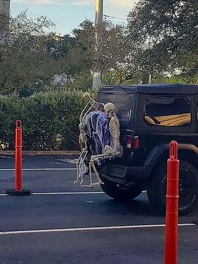 the back of a black jeep, the spare tire of which is decorated with three skeletons of varying sizes, as well as a 'rubber ducky' skeleton