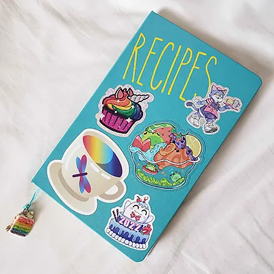 a bright teal Moleskine journal with bright yellow lettering reading 'recipes' and covered in multiple food-related stickers